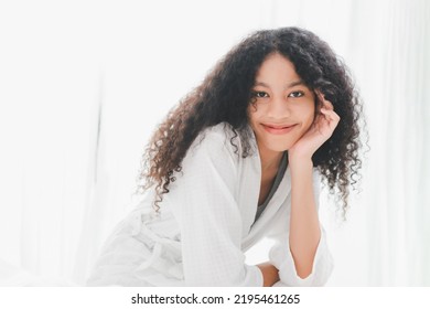 Young Makeup Free Face Mixed Race African American Woman Wearing Bathrobe Sitting On The Bed In Bed Room At Home. Attractive Happy Lady With Healthey No Make Up Bare Skin Face.