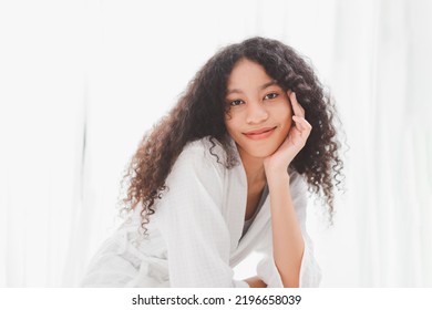 Young Makeup Free Face Mixed Race African American Woman Wearing Bathrobe Sitting On The Bed In Bed Room At Home. Attractive Happy Lady With Healthy No Make Up Bare Skin Face.