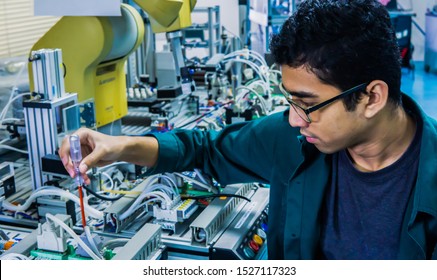 A young Malay engineering student with spectacles working in the lab repairing and troubleshooting an automation machine system using a screwdriver. Image contain noise reduction. Selected focus. - Powered by Shutterstock