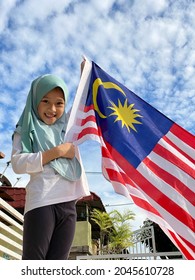 Young Malay Girl Aged 6 Years Old Wearing Turquoise Hijab Smiling While Holding Malaysia Flag During Malaysian Merdeka Day Celebration With Blue Sky As The Background 