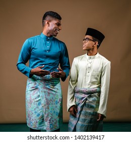 A Young Malay And Indian Men Smile And Laugh As They Stand Next To One Another In A Studio. They Are Both Muslims Preparing To Celebrate Ramadan And Are Both Wearing Traditional Baju Melayu Clothing.