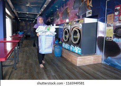 A Young Malay Mother Wearing Hijab Smiling Happily Sending Her Clothes To A Self-service Laundry Shop