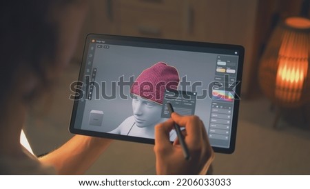 Young male 3D designer working remotely on 3D visualization of clothes in design app using digital tablet computer and stylus