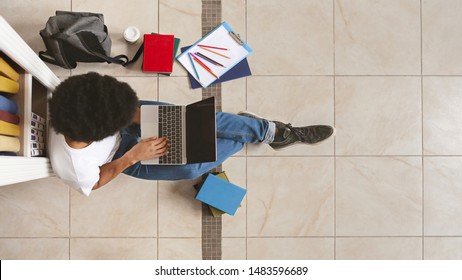 Young Male African American Student Sitting Next To Bookshelf And Using Laptop On Library Floor, Top View, Panorama With Free Space