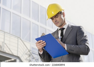 Young male architect writing on clipboard against office building - Powered by Shutterstock