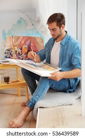 Young male artist painting picture in studio