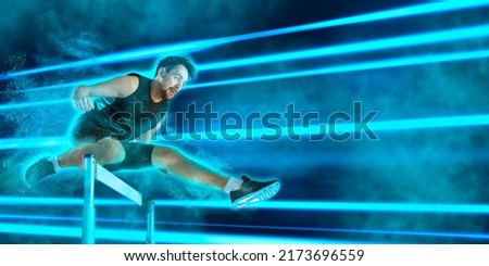 Young male athlete at hurdle race, jumping over the last hurdle. Blue neon background. Sport banner, flyer