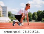 Young male athlete in starting position on a running track outdoors.