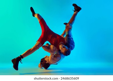 Young male athletes, training wrestling with intensity and focus, aiming to overcome opponent on blue background in neon. Concept of combat sport, martial arts, competition, tournament, athleticism