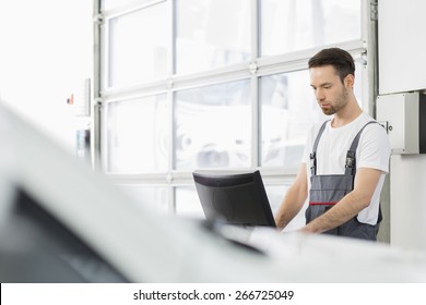 Young Male Automobile Mechanic Using Computer In Repair Shop