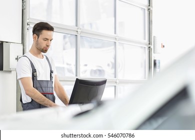 Young Male Automobile Mechanic Using Computer In Repair Shop