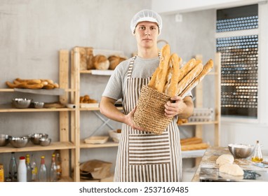 Young male baker in uniform holding basket with fresh baguettes - Powered by Shutterstock