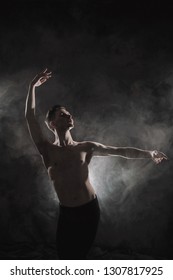 A young male ballet dancer with black leggings and a naked torso performs dance moves against a gray grunge background, with a light of lights and smoke. Conceptual art of contemporary.