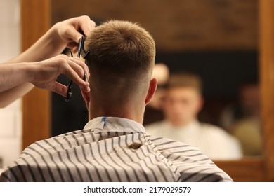 A young male Barber adjusts the hair of a male client. Professional hair care products. Cinematic close-up of a barber giving fade haircut to male client. shot of short clipper hairstyle.