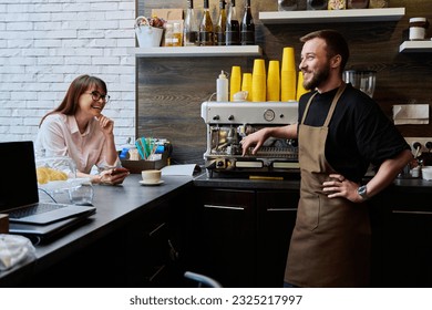 Young male barista talking to woman customer in coffee shop - Powered by Shutterstock