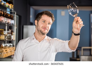 Young Male Bartender Examining Glass Of Wine In Bar