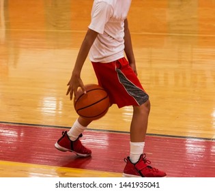 A young male basketball player is dribbling the ball between his legs during basketball camp inside.