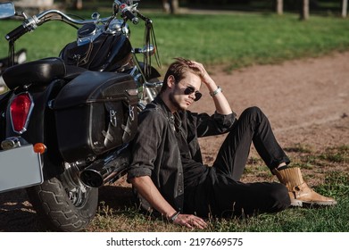 Young Male Biker Sitting On The Ground With His Motor Bike