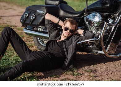 Young Male Biker Sitting On The Ground With His Motor Bike