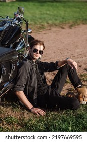 Young Male Biker Sitting On The Ground With His Motor Bike