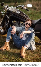 Young Male Biker In Sunglasses Is Sitting On The Groung With A Motor Bike