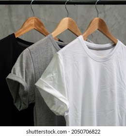 Young Male In Black T-shirt Roll Up Sleeves Template, Three Color Black White Gray Tee Wooden Hanger On Cement Background For Man Design Mockup Concept Man Tshirt Product, Woman Shirt Wearing.