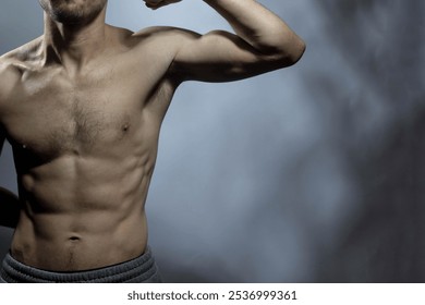 A young male body with well-defined abs and chest. Model flexing biceps with shirtless torso. Concept of body care, male health, fitness, youth, masculinity, health, weightloss, bodybuilding  - Powered by Shutterstock