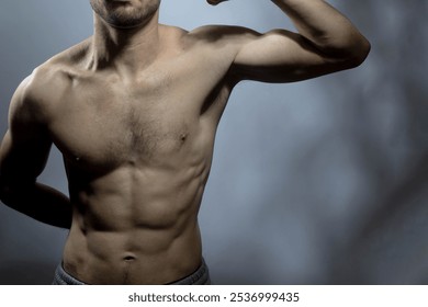 A young male body with well-defined abs and chest. Model flexing biceps with shirtless torso. Concept of body care, male health, fitness, youth, masculinity, health, weightloss, bodybuilding  - Powered by Shutterstock