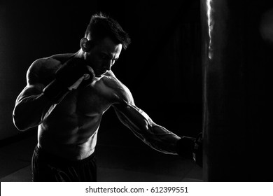 Young Male Boxer Hitting Punching Bag On Black Background.