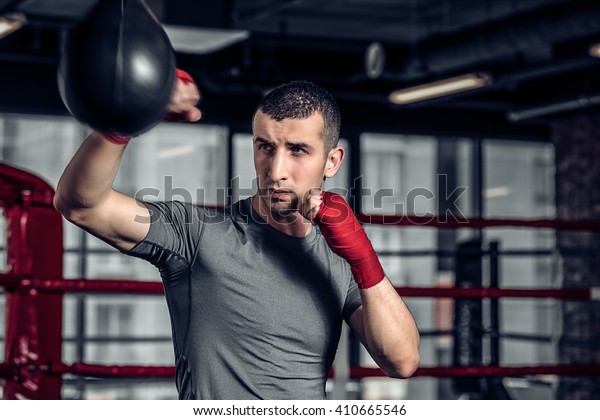 Young Male boxer using a punching bag in gym.\
Boxer hitting punching speed bag in gym, head and shoulders.\
Athlete with red boxing\
bandages.