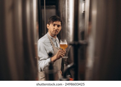 Young male brewer holding a glass of beer in hand Eating craft beer to check the taste and color of the beer in the craft brewery. - Powered by Shutterstock