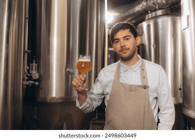 Young male brewer holding a glass of beer in hand Eating craft beer to check the taste and color of the beer in the craft brewery. - Powered by Shutterstock