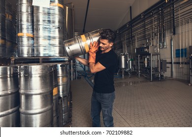 Young male brewer with keg at brewery factory warehouse. Young man working at warehouse in brewery. Arranging metal beer barrel. - Powered by Shutterstock