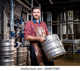 Young male brewer in leather apron holds barrel with craft beer at modern brewery factory - Powered by Shutterstock