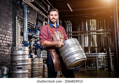 Young male brewer in leather apron holds barrel with craft beer at modern brewery factory - Powered by Shutterstock