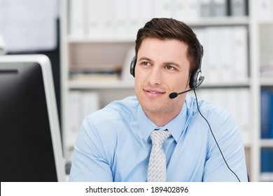 Young male call centre operator sitting wearing a headset sitting listening to a conversation with a pensive thoughtful expression