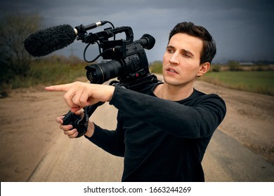 young male cameraman give instructions to someone with finger to side and camera an his shoulder directing while video shoot