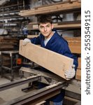 Young male carpenter putting wooden board on cutting machine in wood workshop