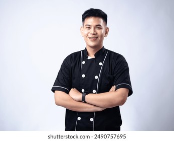 Young male chef in a black uniform standing confidently with arms crossed, smiling. The chef's confident and approachable demeanor, combined with his professional attire - Powered by Shutterstock