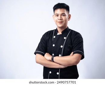 Young male chef in a black uniform standing confidently with arms crossed, smiling. The chef's confident and approachable demeanor, combined with his professional attire - Powered by Shutterstock