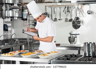 Young male chef with clipboard going through cooking checklist at commercial kitchen counter - Powered by Shutterstock