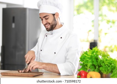 Young Male Chef Cutting Meat In Kitchen