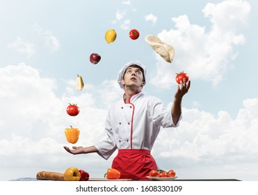 Young male chef juggles with food ingredients. Handsome chef in white hat and red apron on blue sky background. Professional cooking classes advertising. Food retail campaign announcement. - Powered by Shutterstock