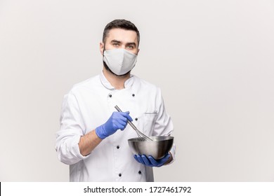 Young Male Chef In Uniform, Protective Mask And Gloves Mixing Milk And Raw Eggs In Metallic Bowl While Cooking Food For Clients Of Restaurant