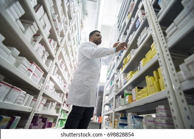 Young Male Chemist Arranging Products In Shelves At Pharmacy