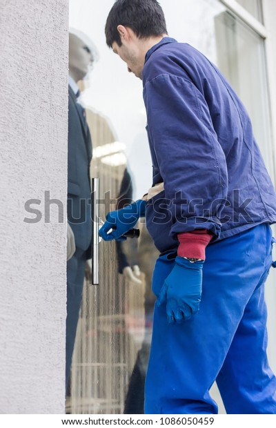 A young male cleaner in blue overalls\
washes windows and store front. Cleaning\
Service