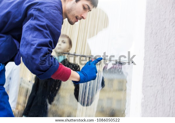 A young male cleaner in blue overalls\
washes windows and store front. Cleaning\
Service