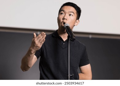 A young male college student is confidently standing in front of a microphone and gesturing while giving a speech during a public speaking competition - Powered by Shutterstock