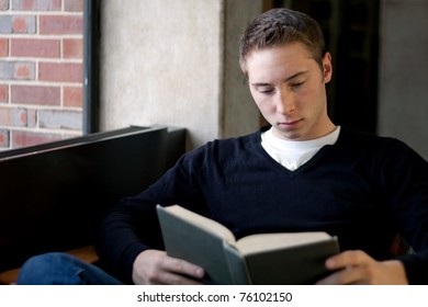 A Young Male College Student Reads A Book At The Library.