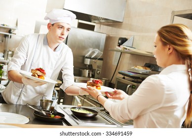 young male cook chef in white uniform gives to waitress plates with prepared meal in commercial kitchen - Powered by Shutterstock